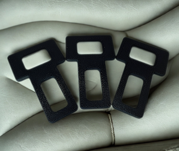 Three black seat belt buckles on a beige leather surface